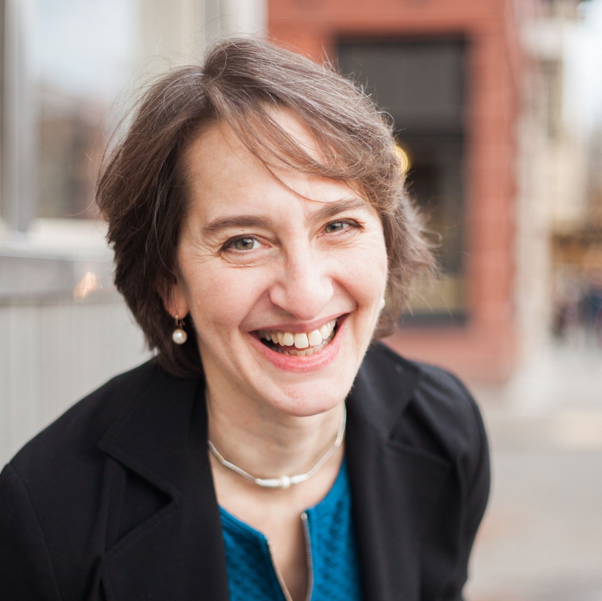 A woman in a blue shirt and black jacket is smiling for the camera.