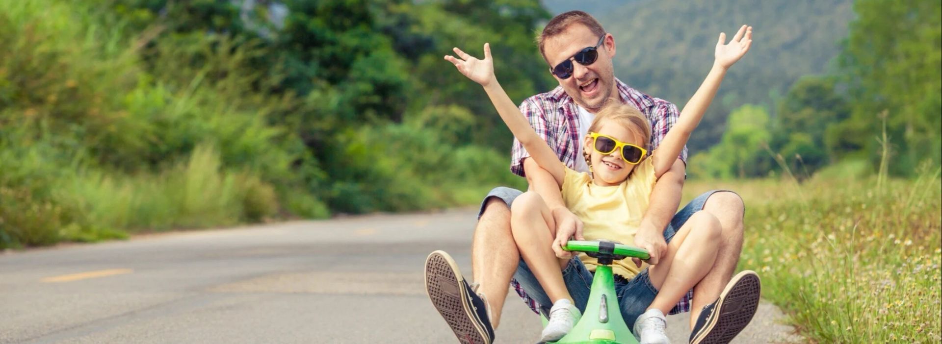 A man and a little girl are riding a toy car down a road.
