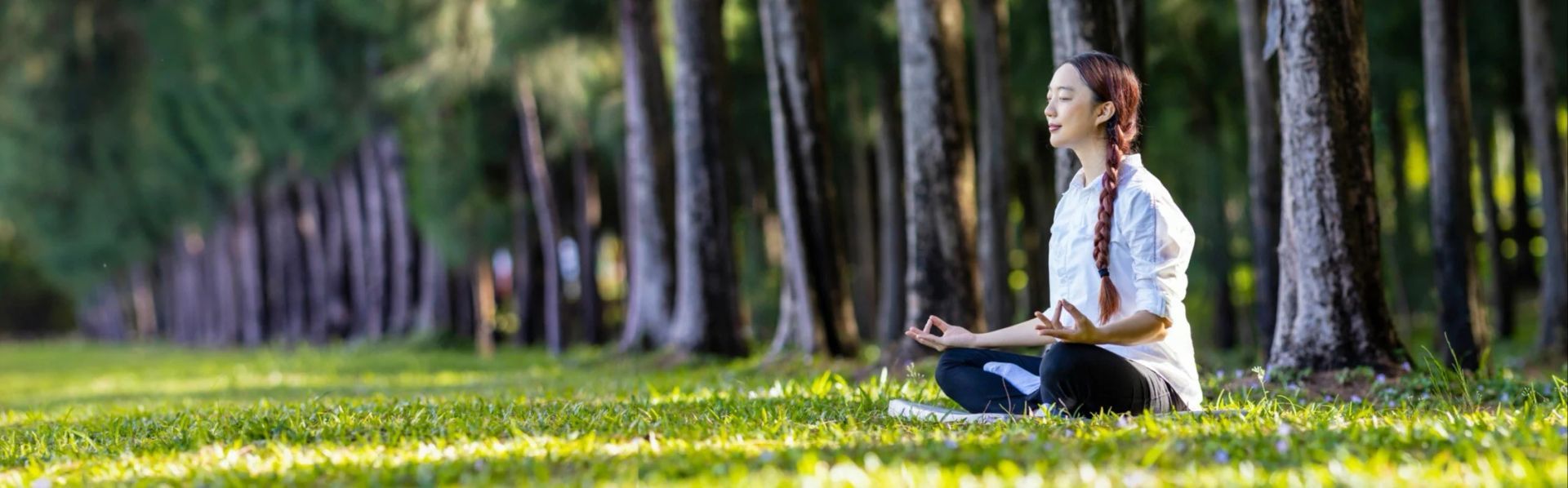 A woman is sitting in a lotus position in the middle of a forest.