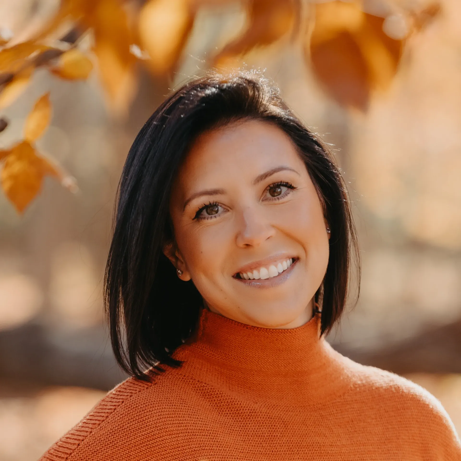 A woman wearing an orange sweater is smiling for the camera
