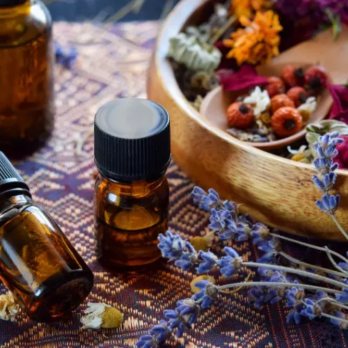 A bottle of essential oil is sitting next to a bowl of dried flowers.