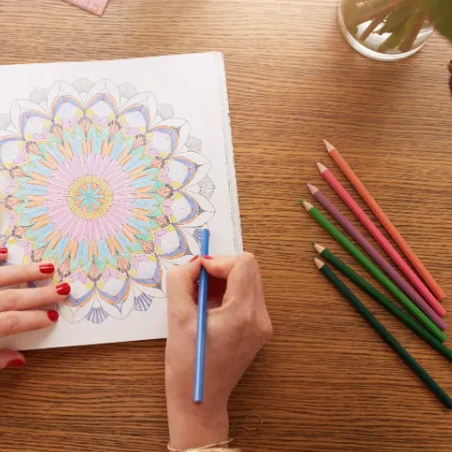 A person is drawing a mandala with colored pencils on a wooden table.