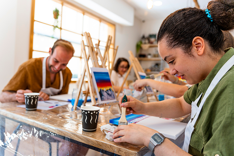 A group of people are sitting at a table painting.