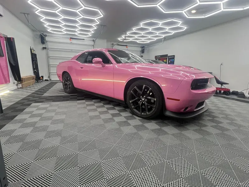 Pink Dodge Challenger in a garage with black flooring and hexagon lights.