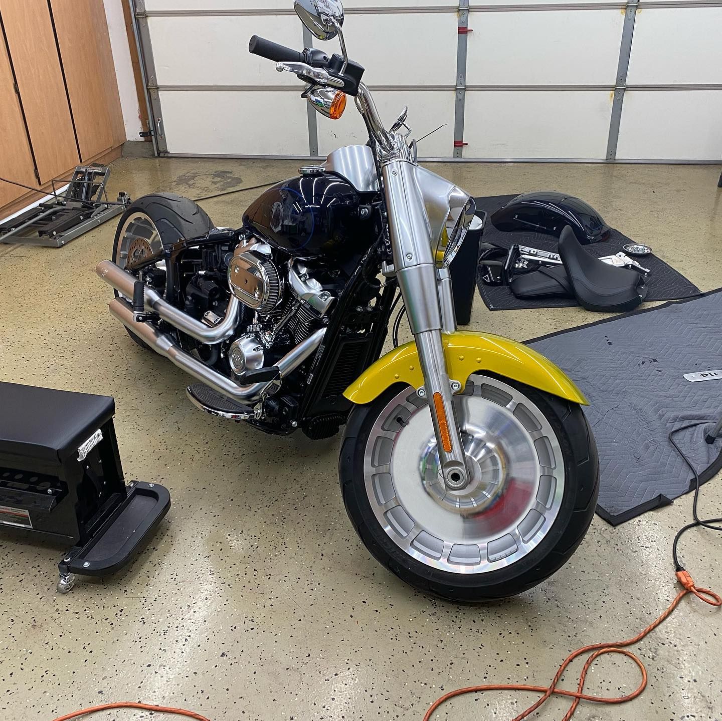 Black and yellow Harley-Davidson motorcycle in a garage with parts on the floor.