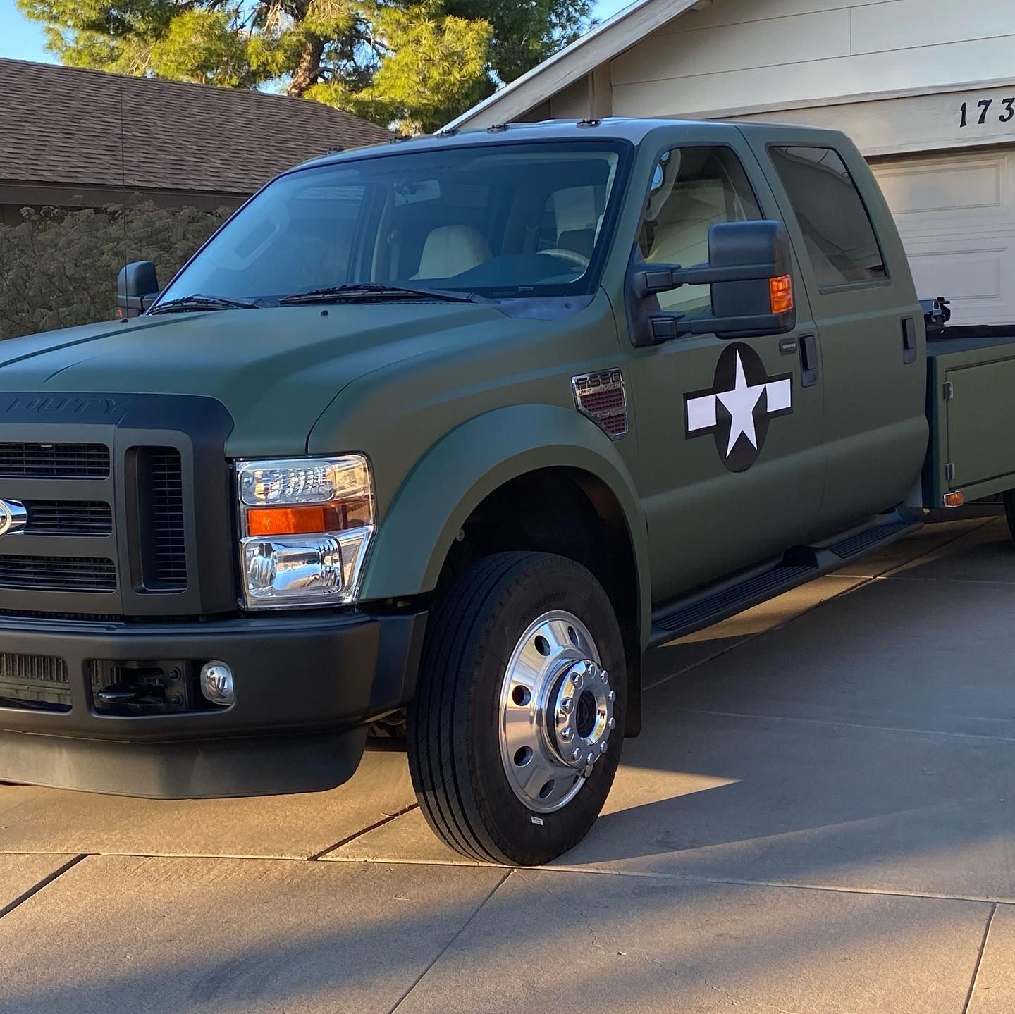 Olive green Ford pickup truck with a white star emblem on the door, parked in a driveway.