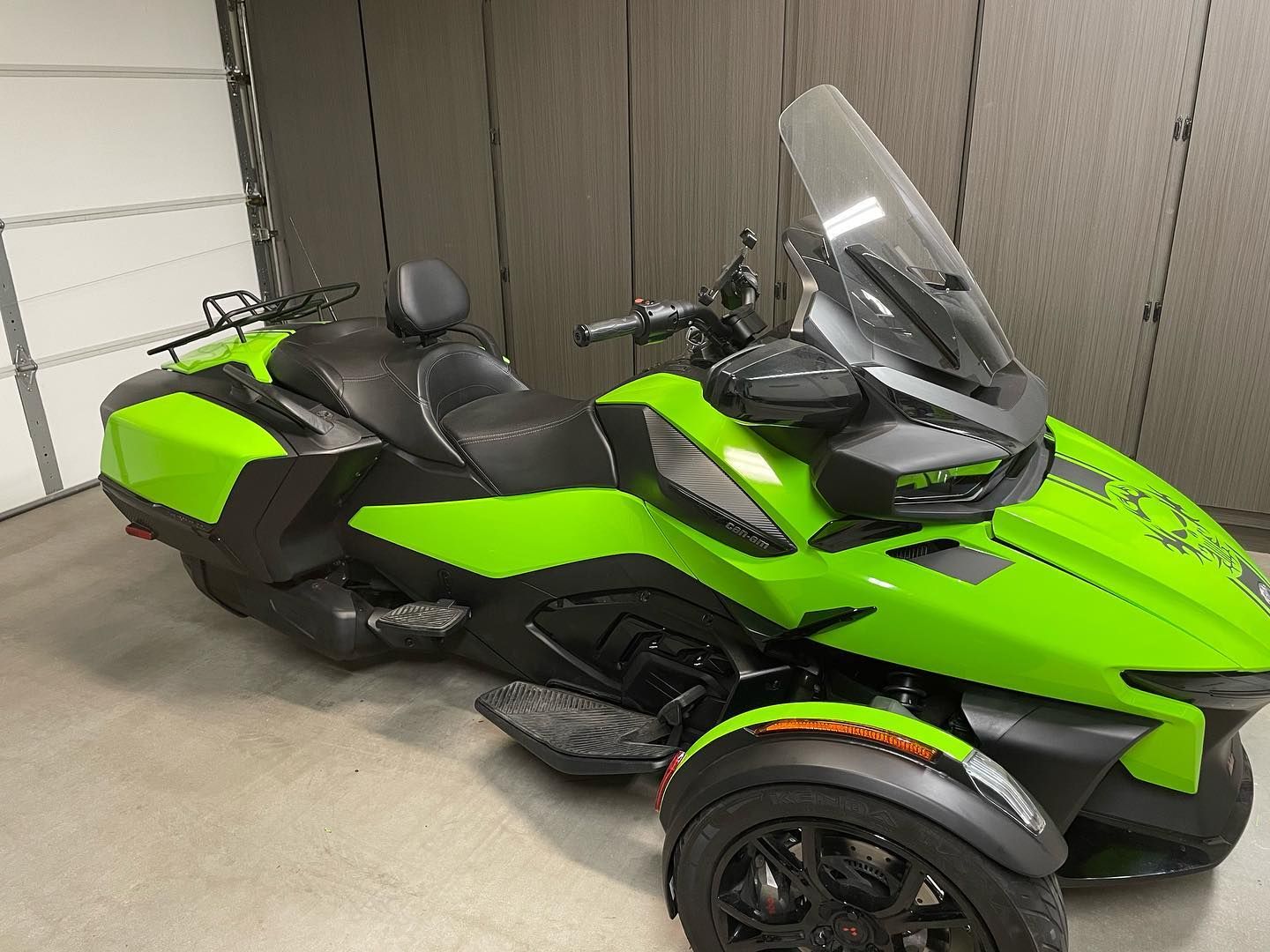 Green and black three-wheeled motorcycle with a windshield, parked indoors.