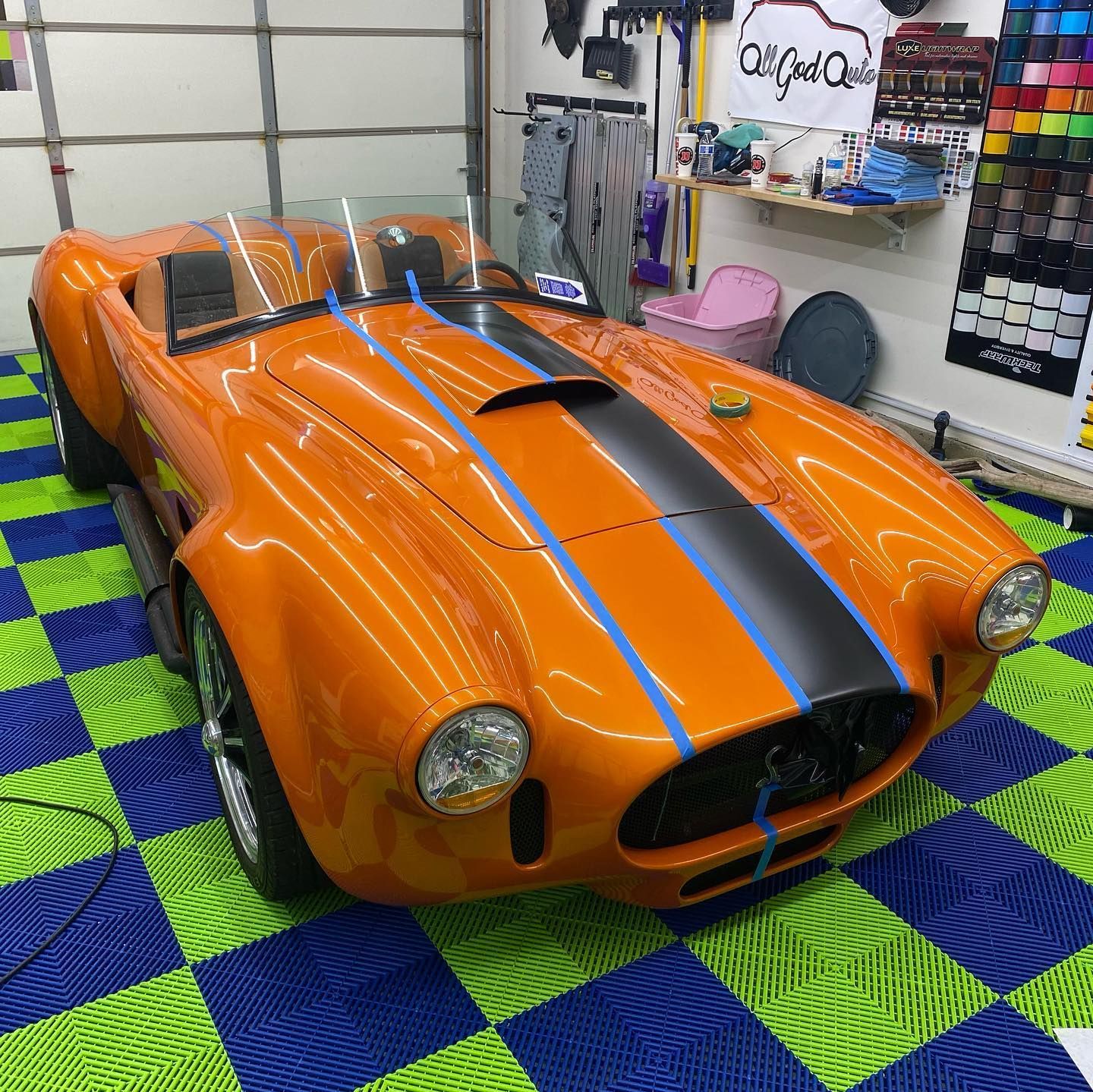 Orange Cobra sports car with black stripe in a garage with checkered floor.