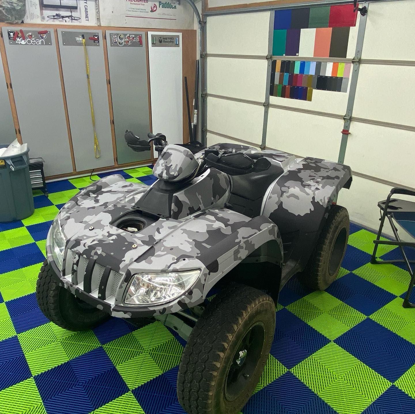 An ATV with a gray and white camouflage design parked in a garage with a checkered floor and a color swatch display.