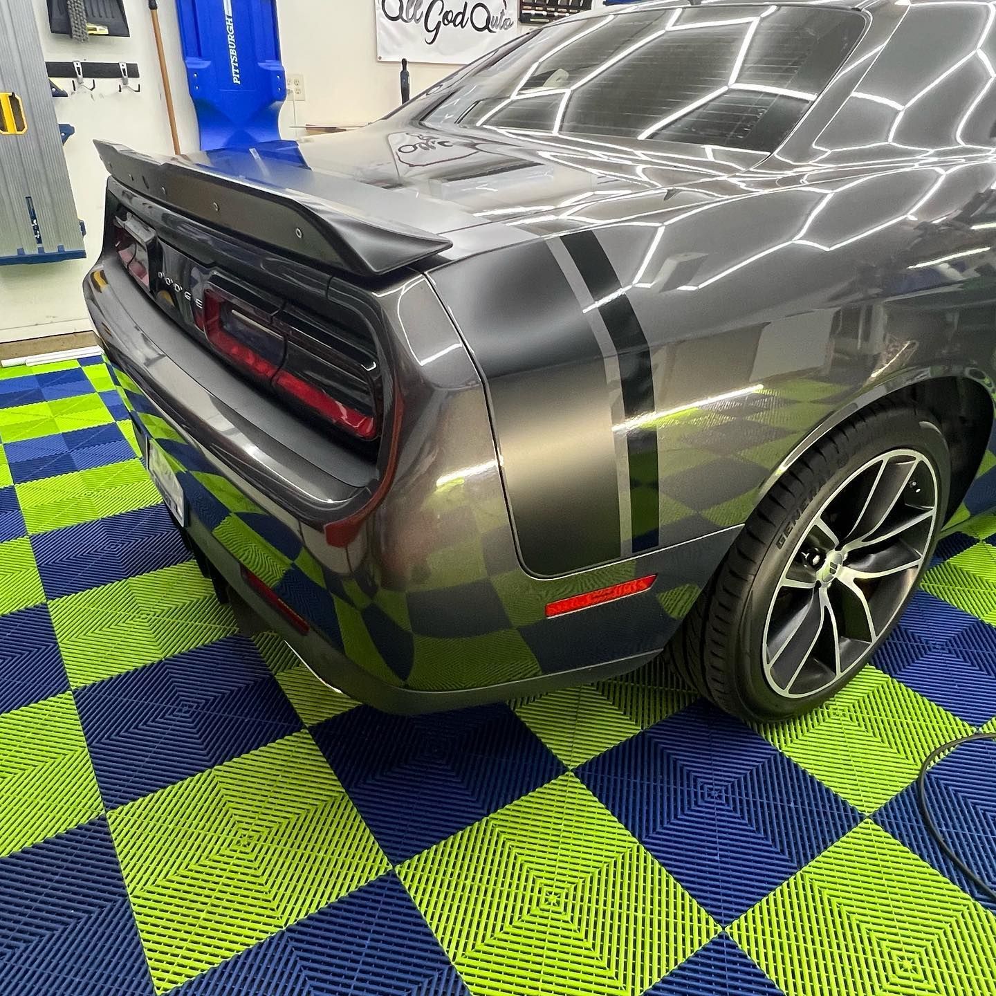 Grey Dodge Challenger with black stripes on green/blue checkered floor.