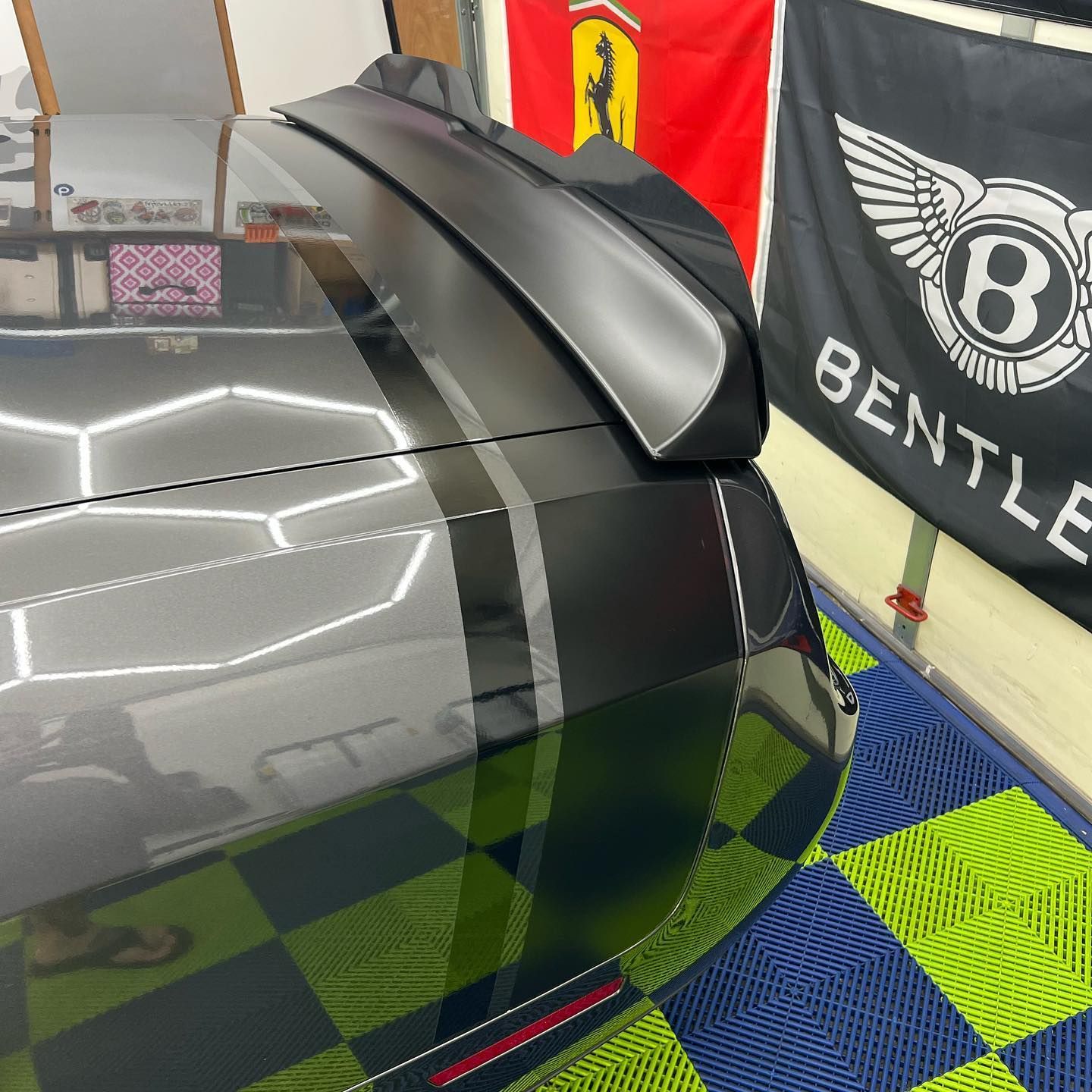 Dark gray car with racing stripes and spoiler, inside a garage with flags.