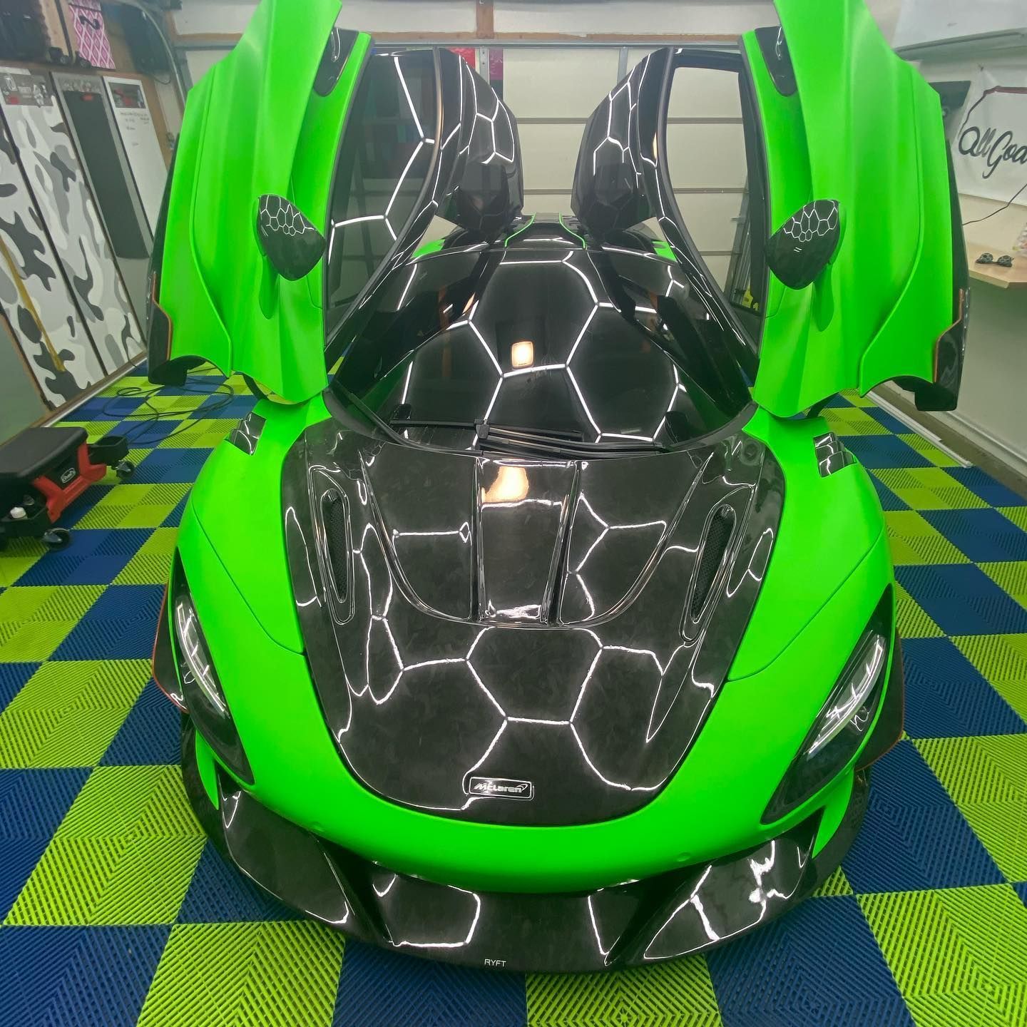 Bright green sports car with open doors, black carbon fiber hood, on a checkered floor.