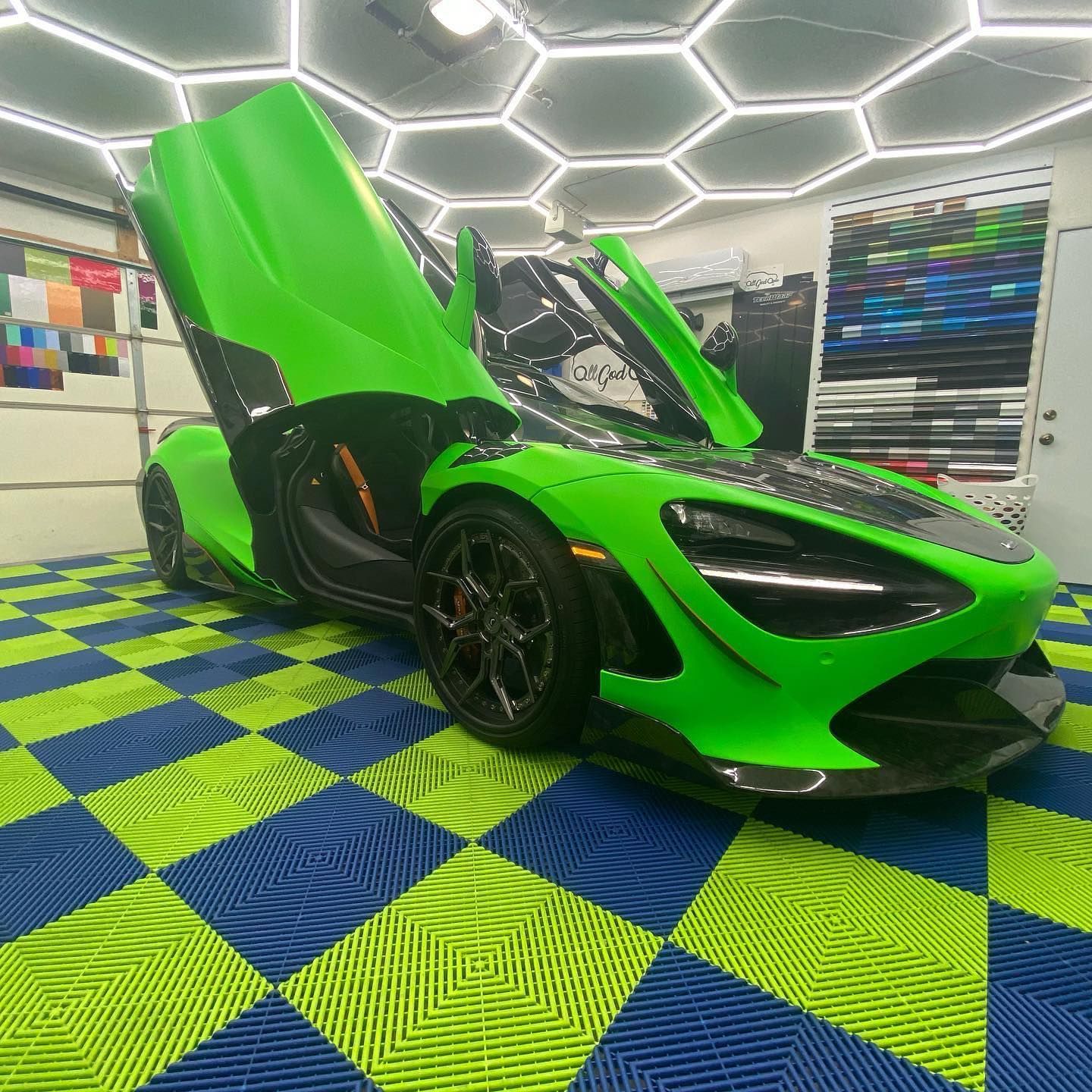 Green McLaren sports car with doors open, parked on a checkered floor.