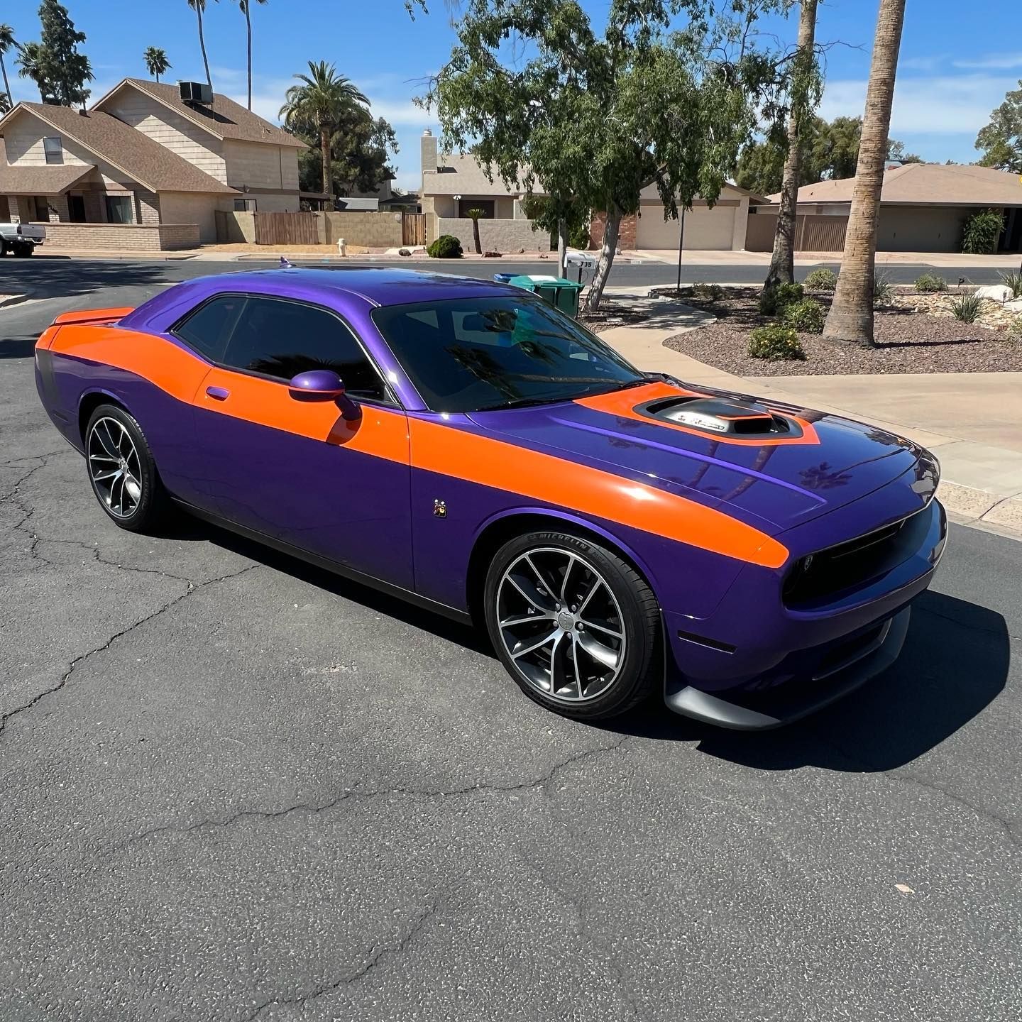 Purple and orange Dodge Challenger parked on a street in a residential area on a sunny day.