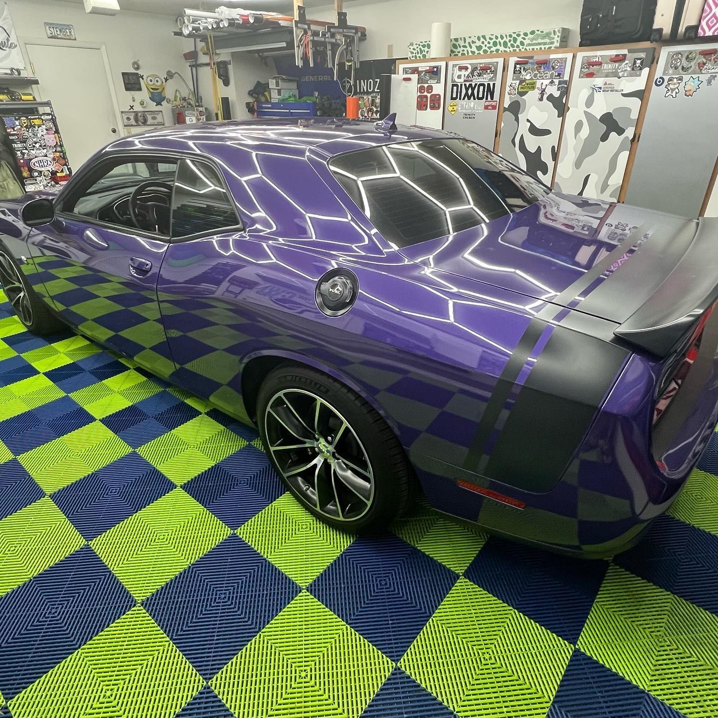 Purple Dodge Challenger with black stripes on a checkered blue and green floor in a garage.