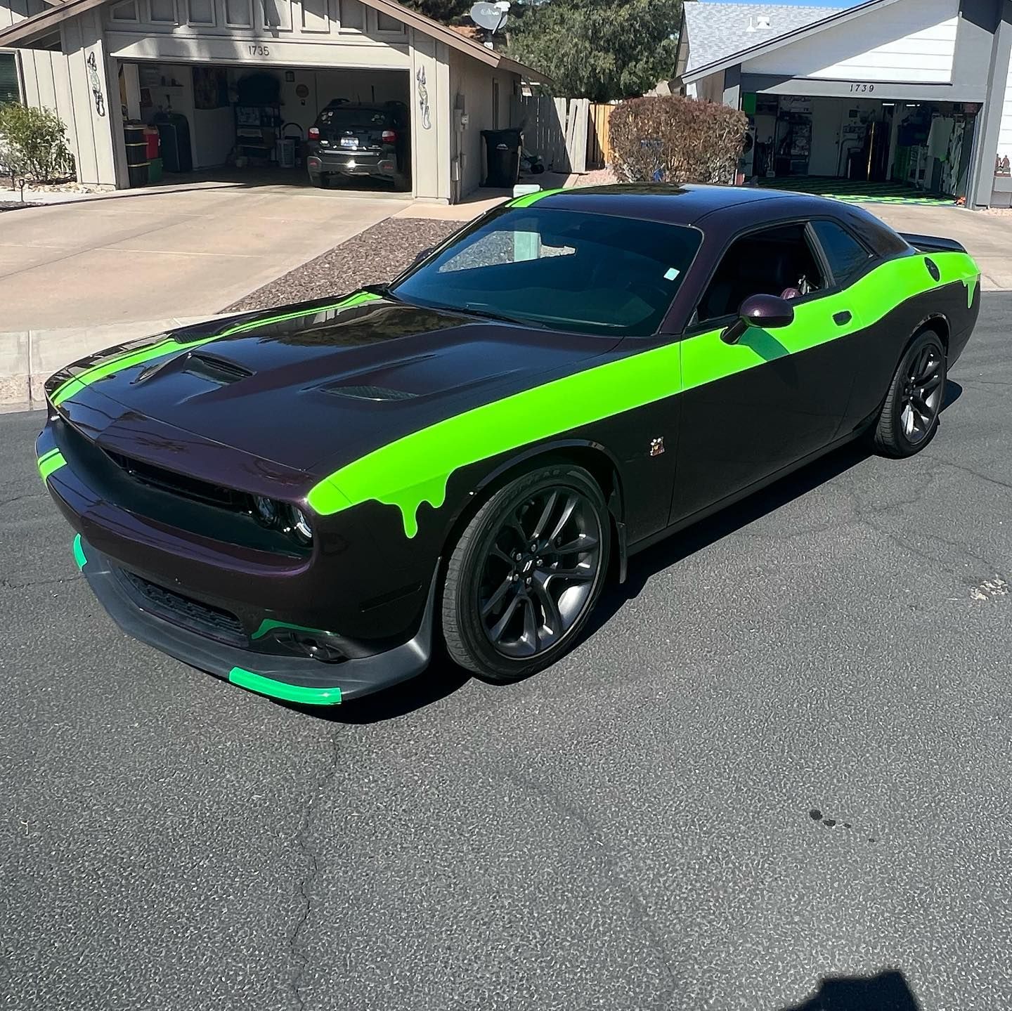 Dark car with neon green stripes, parked on a street in front of houses.