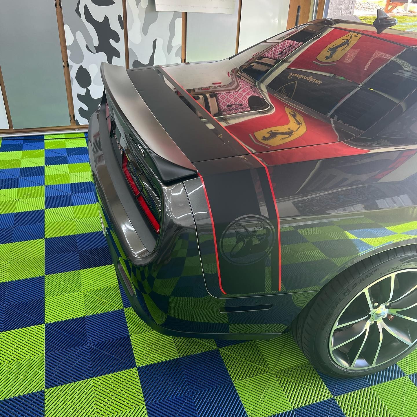 A dark gray Dodge Challenger with red racing stripes on a checkered blue and green floor.