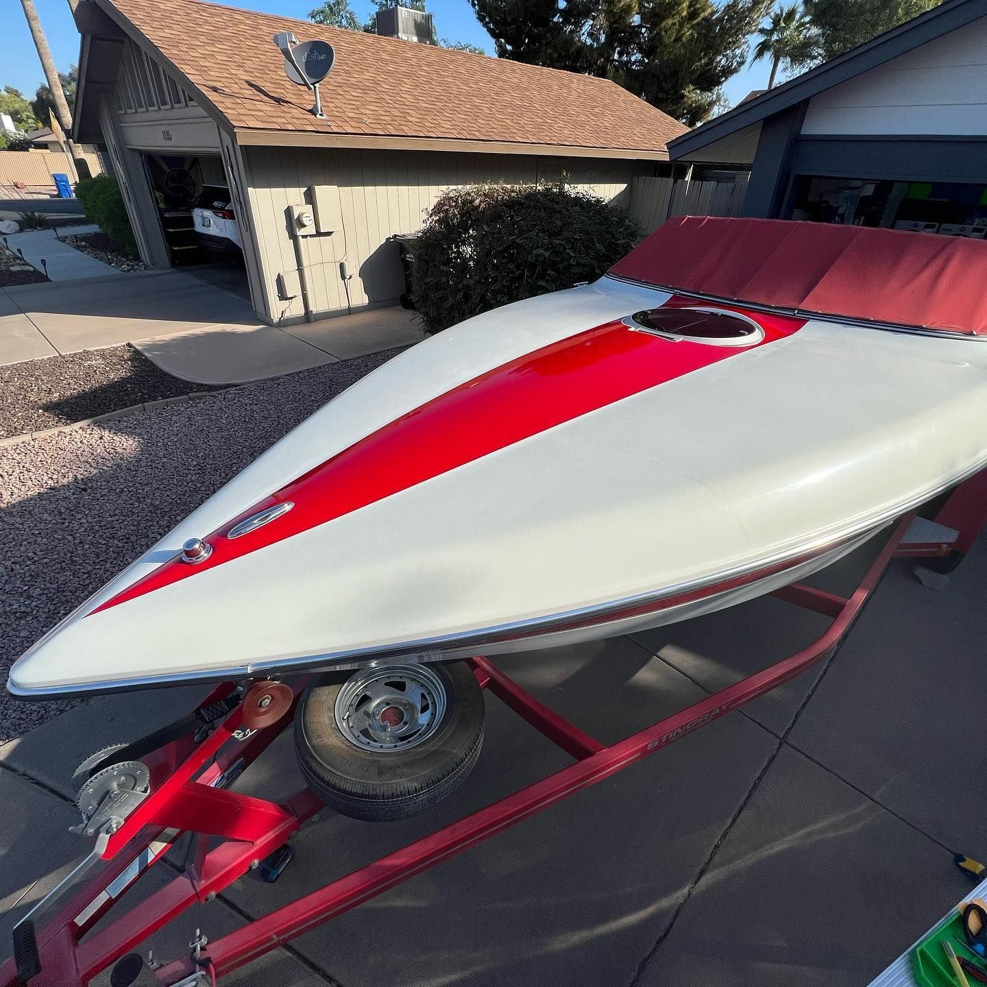 White and red speedboat on a red trailer parked on a driveway in front of a house.