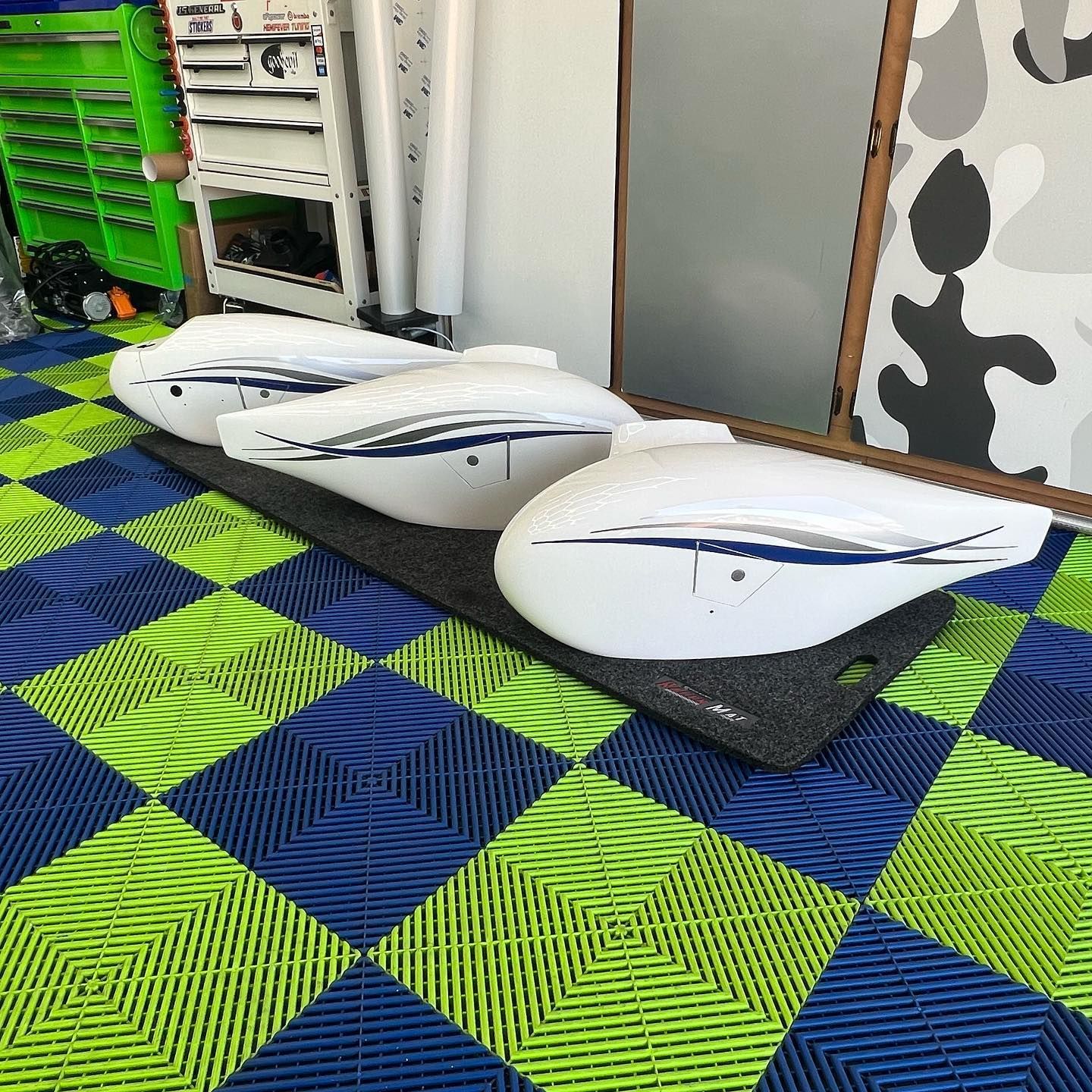 Three white boat seats with blue and gray accents on black padding, indoors on checkered floor.