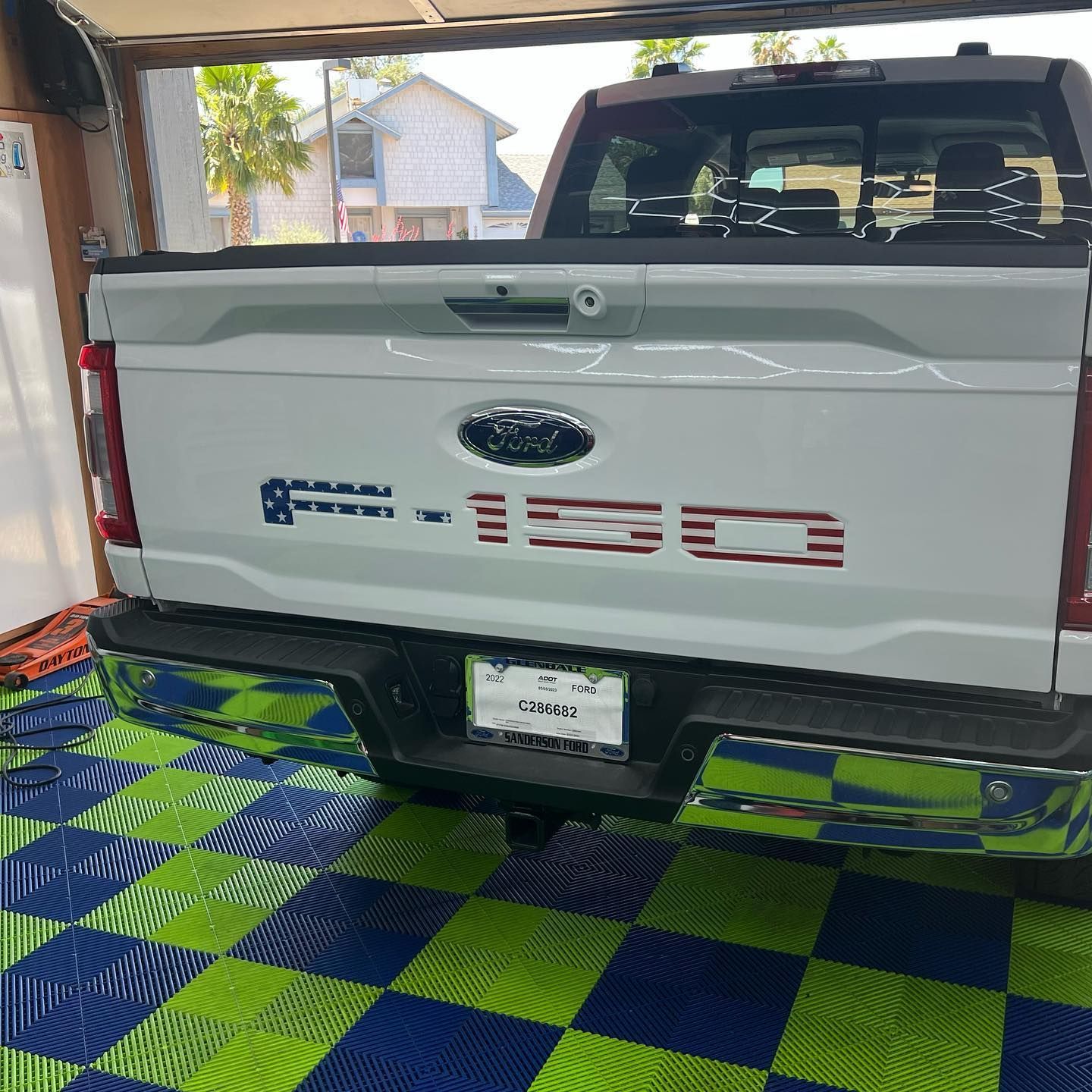 White Ford F-150 truck with American flag-themed stickers on the tailgate, parked on a tiled floor.
