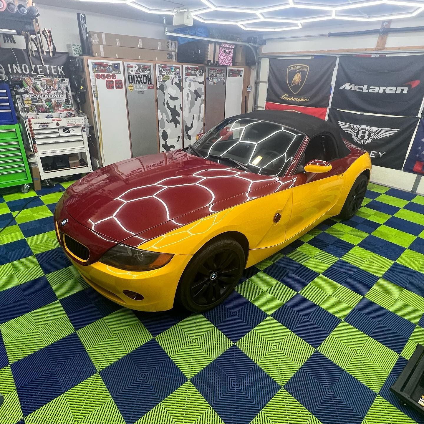 BMW Z4 convertible in burgundy and yellow in a garage with checkered floor.