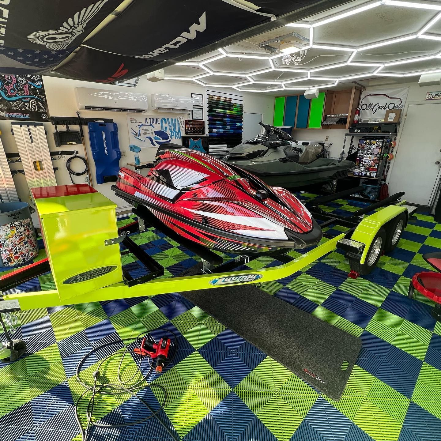 Red and black jet ski on a lime green trailer in a garage with a tiled floor.
