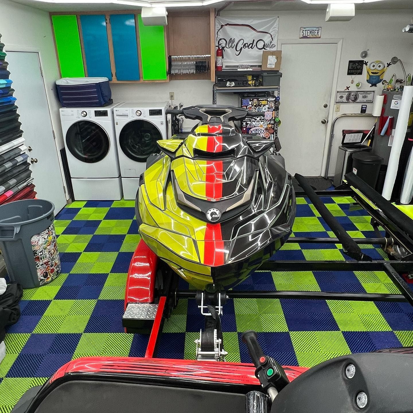 Snowmobile with yellow, black, and red design on trailer, in garage with washer/dryer.