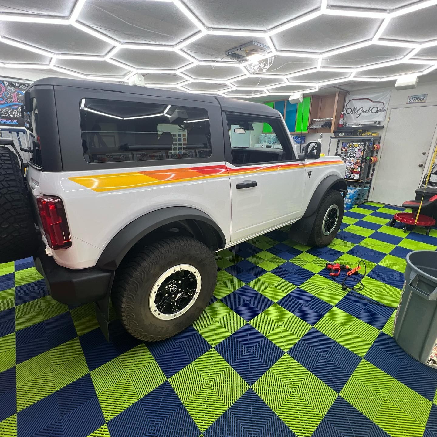 White Ford Bronco with colorful side stripes parked indoors on a blue/green checkered floor.