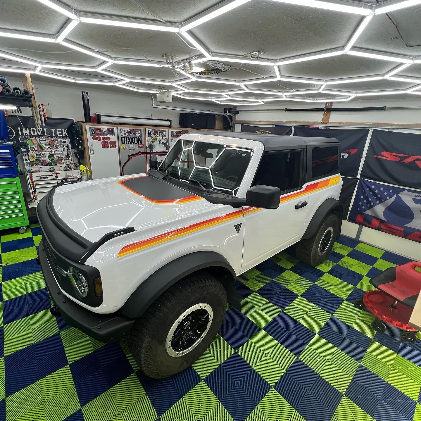 White Ford Bronco with retro stripes in garage with hexagonal lights and checkered floor.