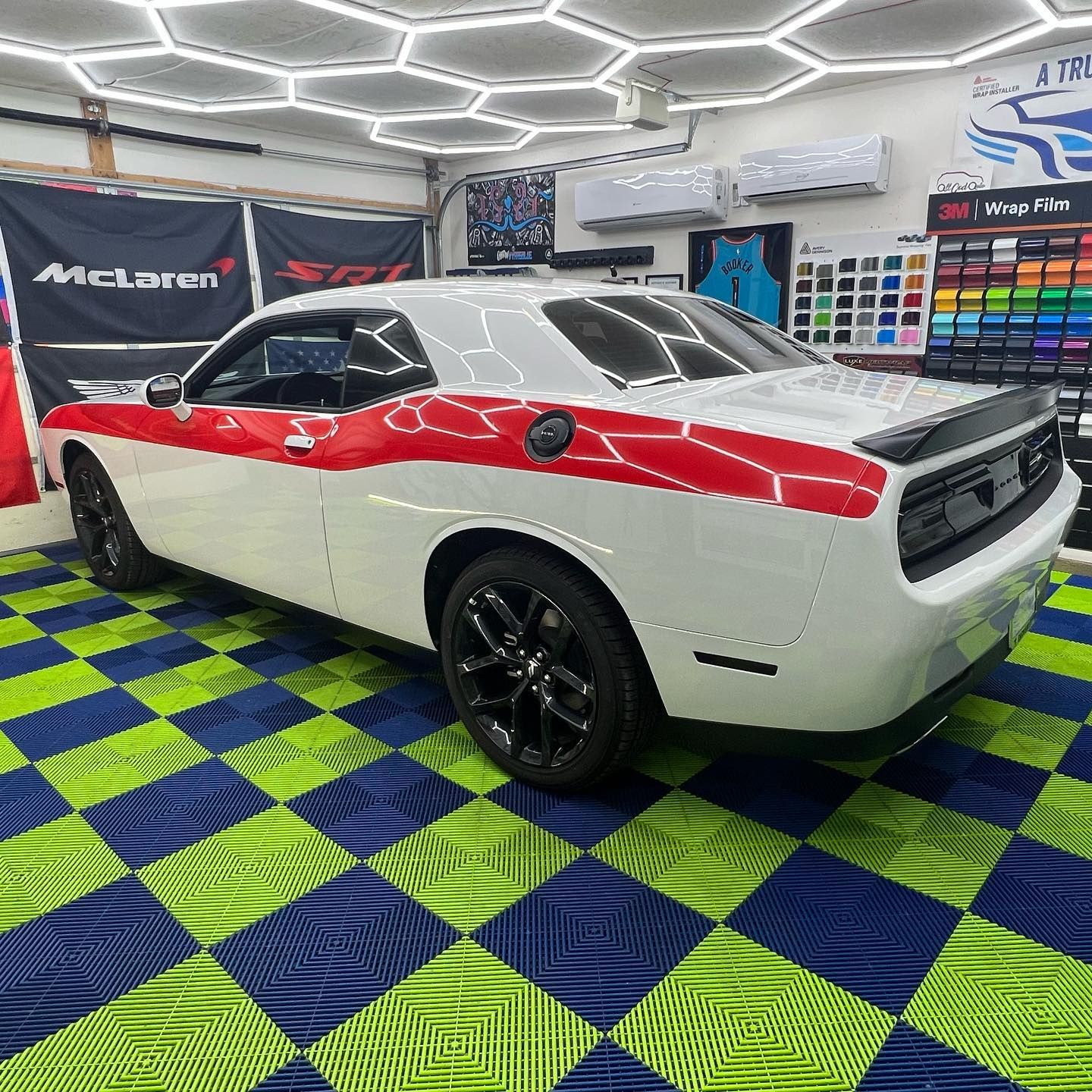 Dodge Challenger with red stripe in a garage with patterned floor and hexagonal ceiling lights.