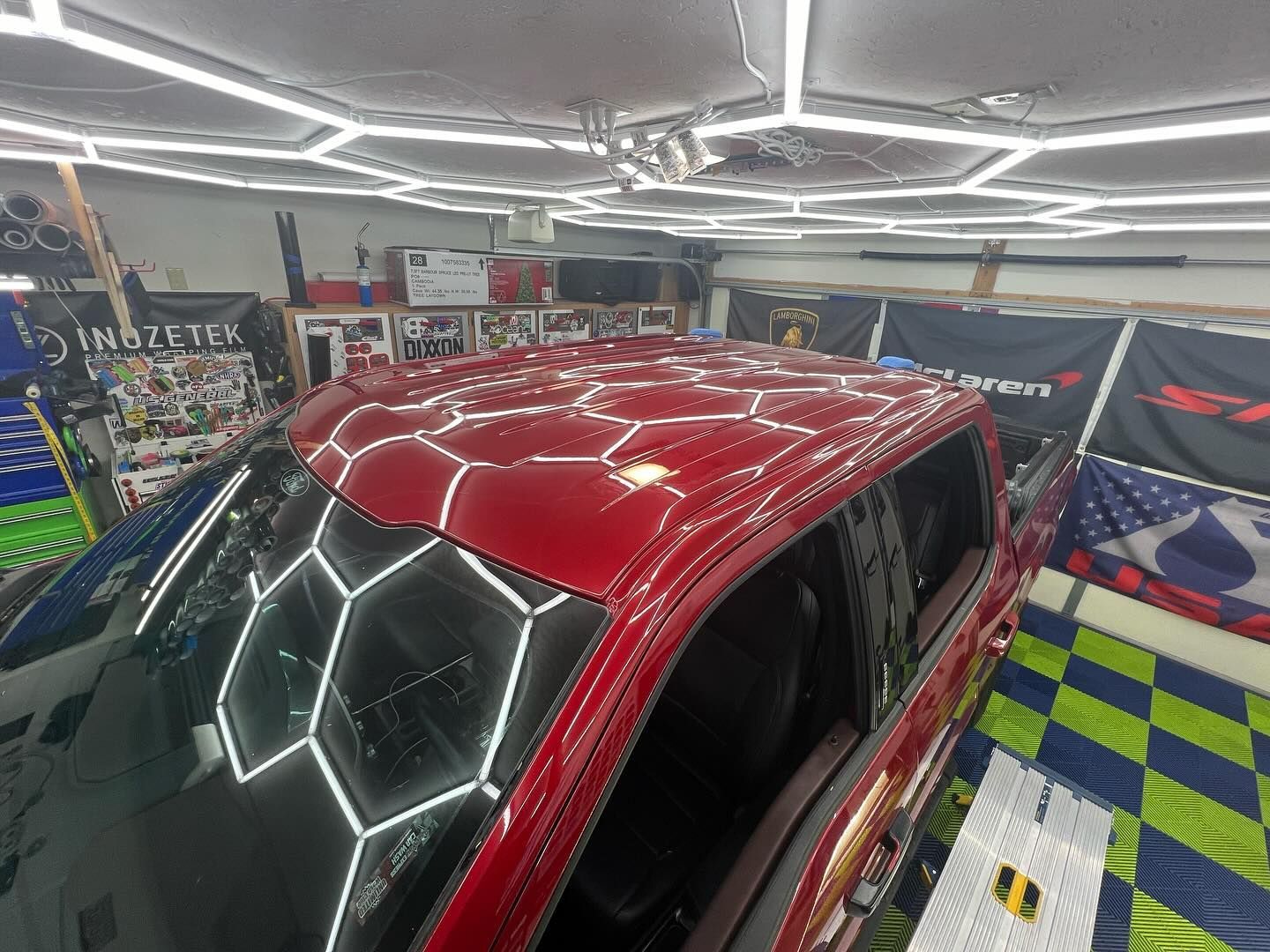 Red pickup truck under hexagon-shaped lights, reflecting on its shiny roof in a shop setting.