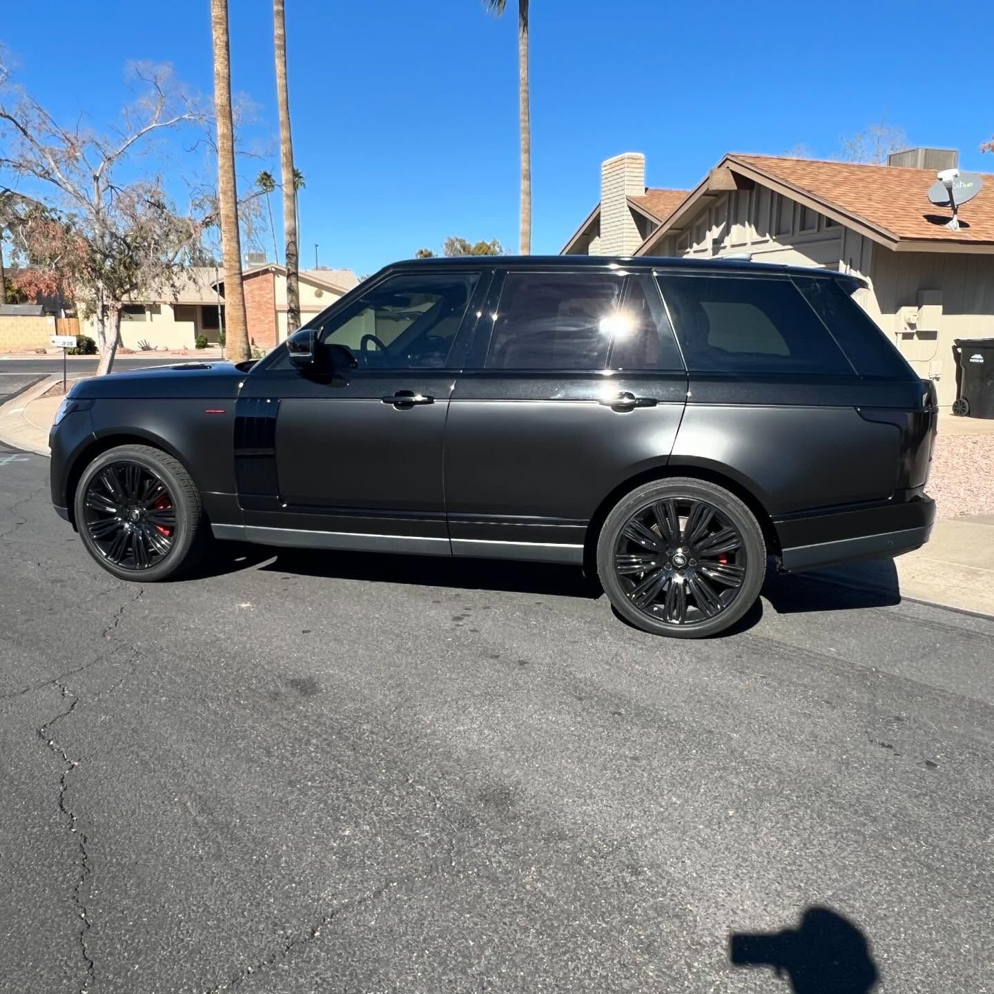Black Range Rover parked on a residential street with black rims, against a clear blue sky.