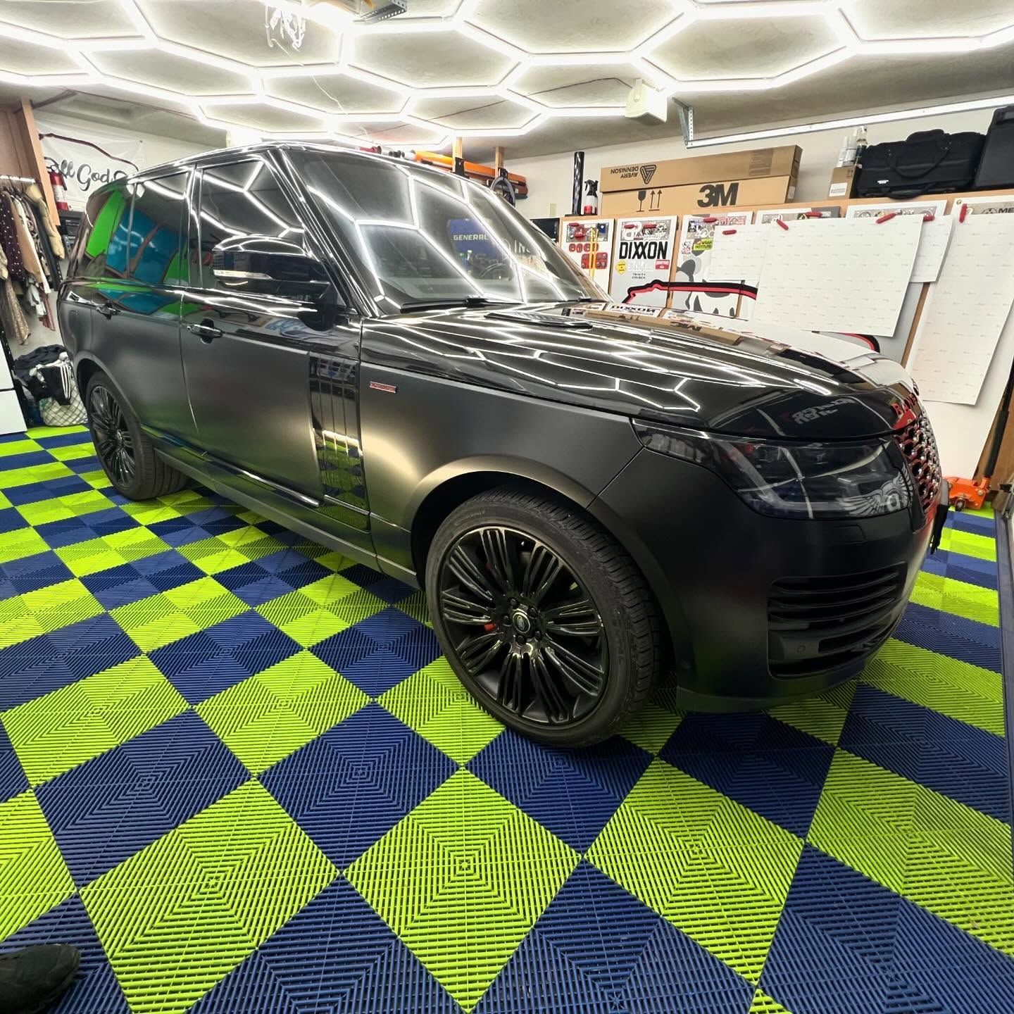 Black Range Rover SUV parked on a patterned blue and green floor inside a workshop.