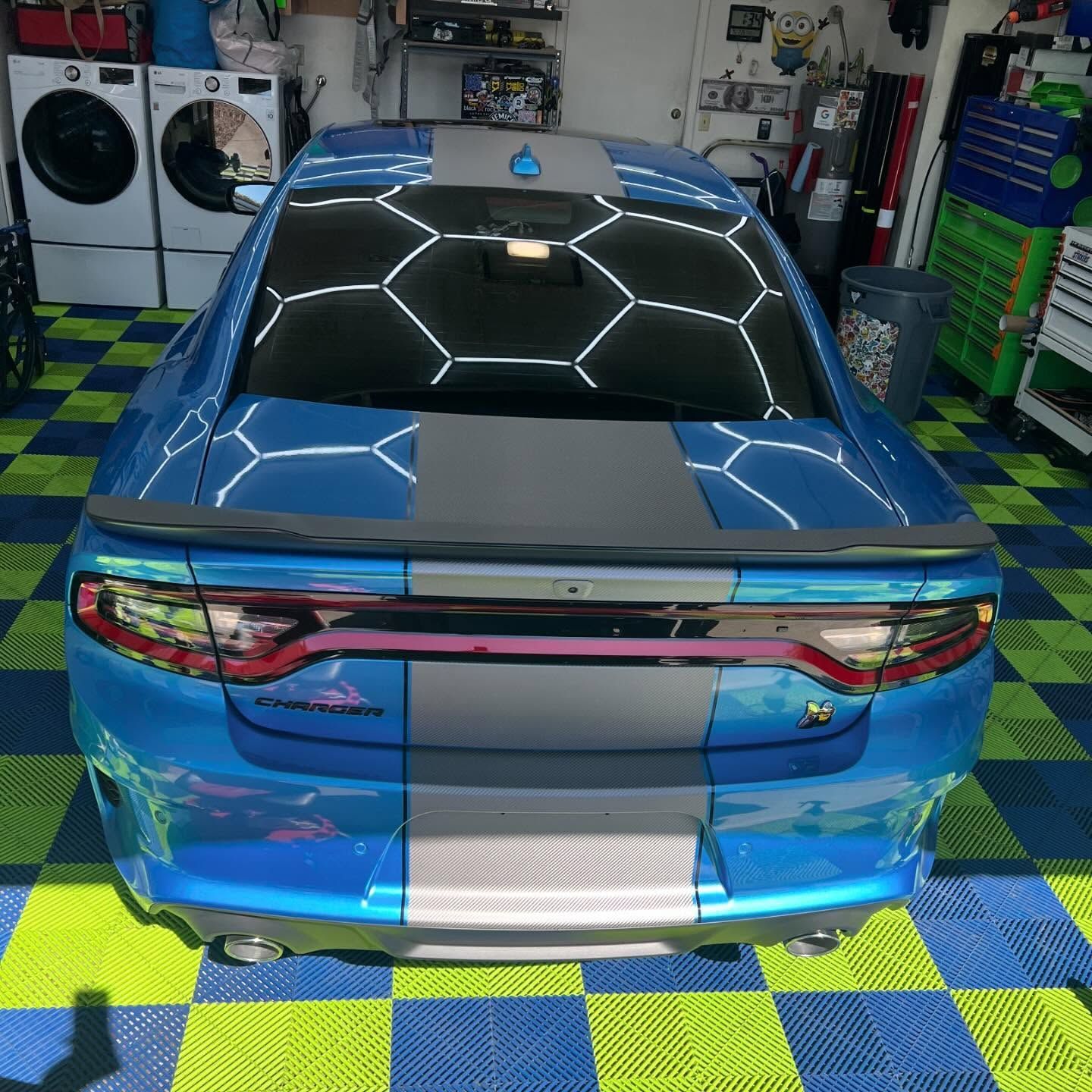 Blue Dodge Charger with gray racing stripes parked in a garage with a checkered floor.