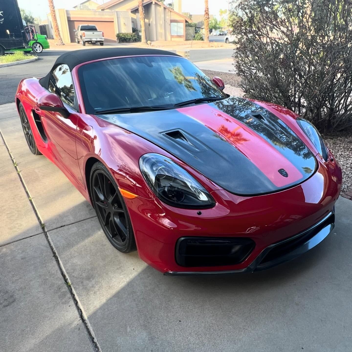 Red Porsche convertible with black racing stripes, parked on a driveway.