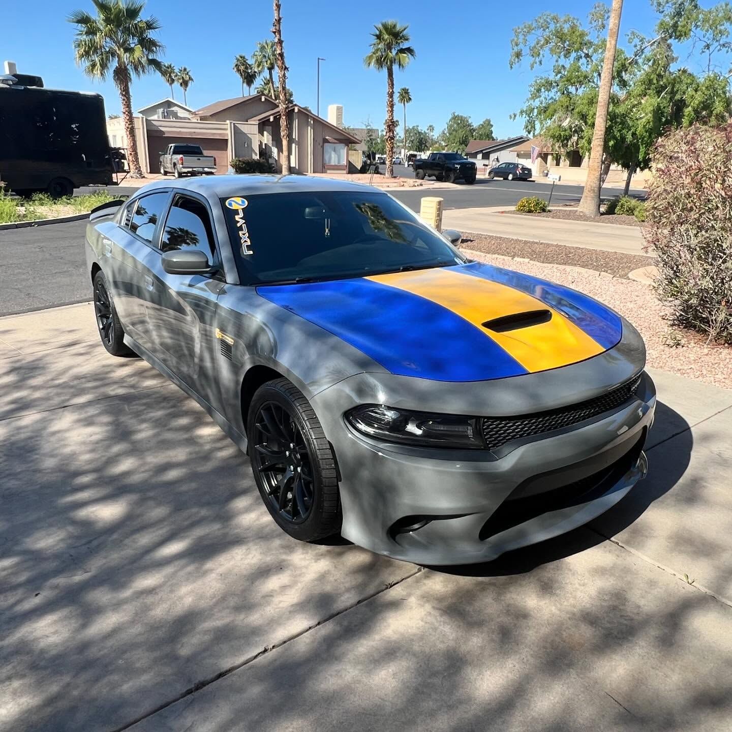 Gray Dodge Charger with a blue and yellow hood parked on a driveway.