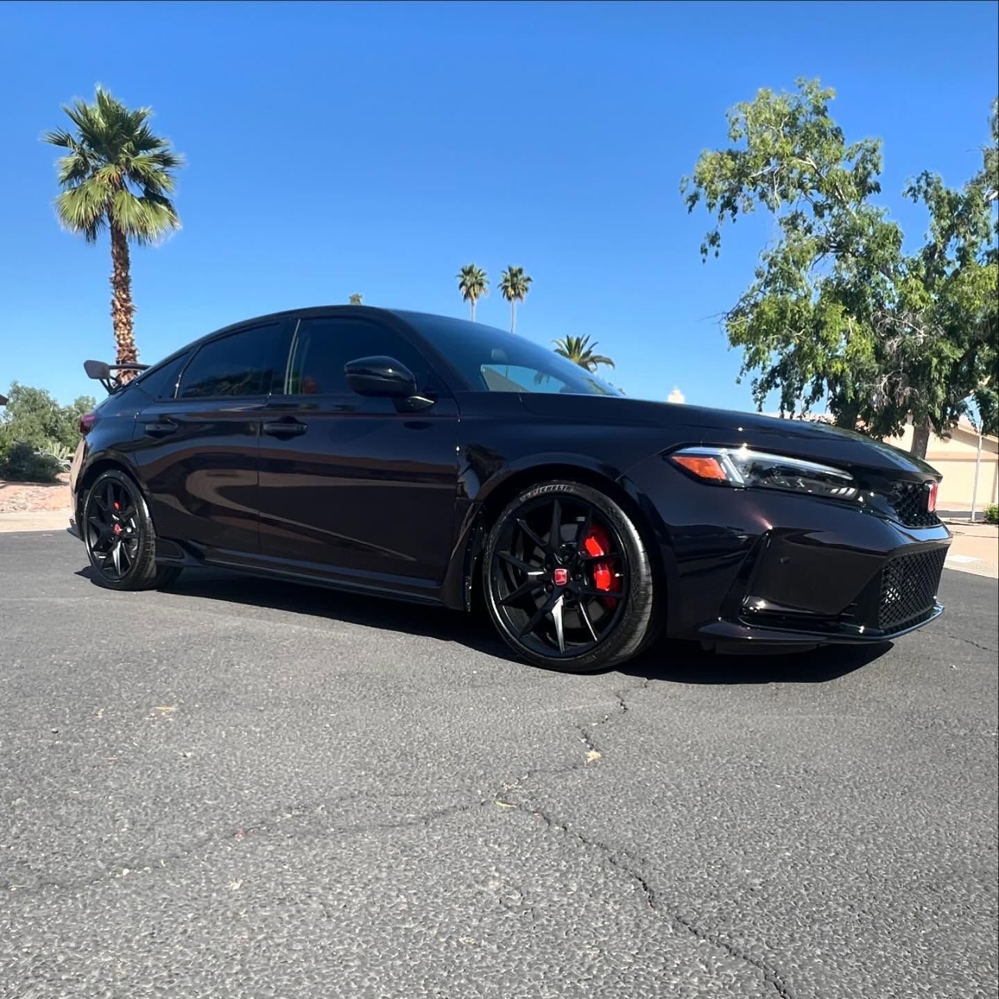 Dark sedan parked on pavement with palm trees and blue sky.