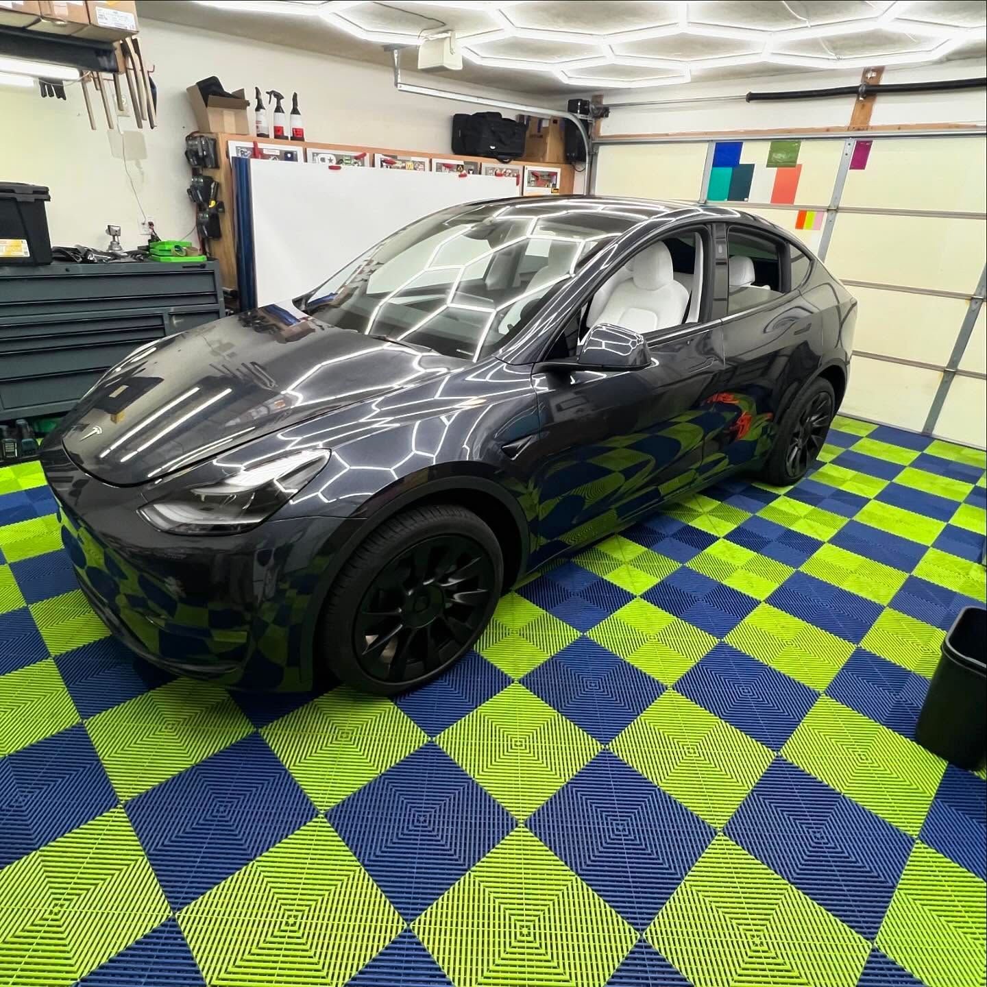 Dark gray Tesla SUV parked on a checkered blue and green garage floor.