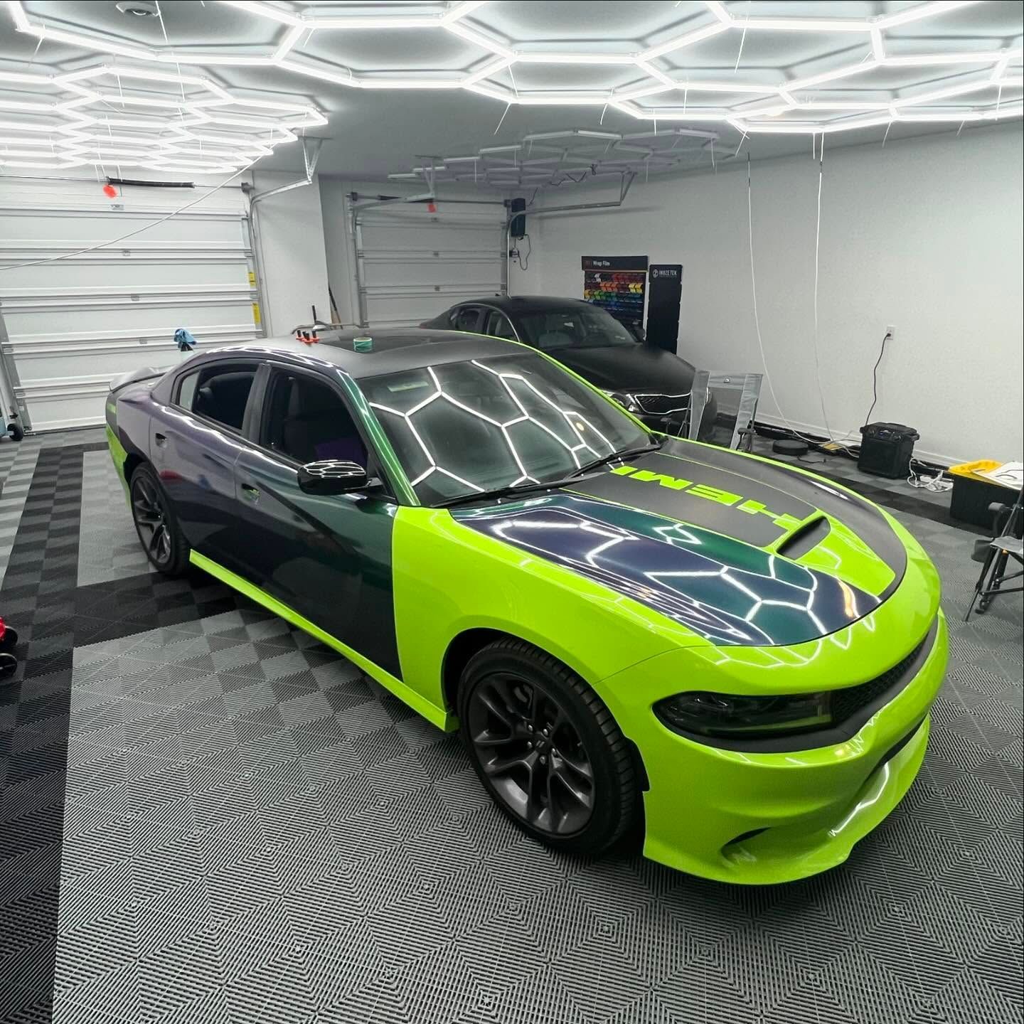 Bright green and dark blue custom Dodge Charger in a garage with patterned floor and hexagon lights.