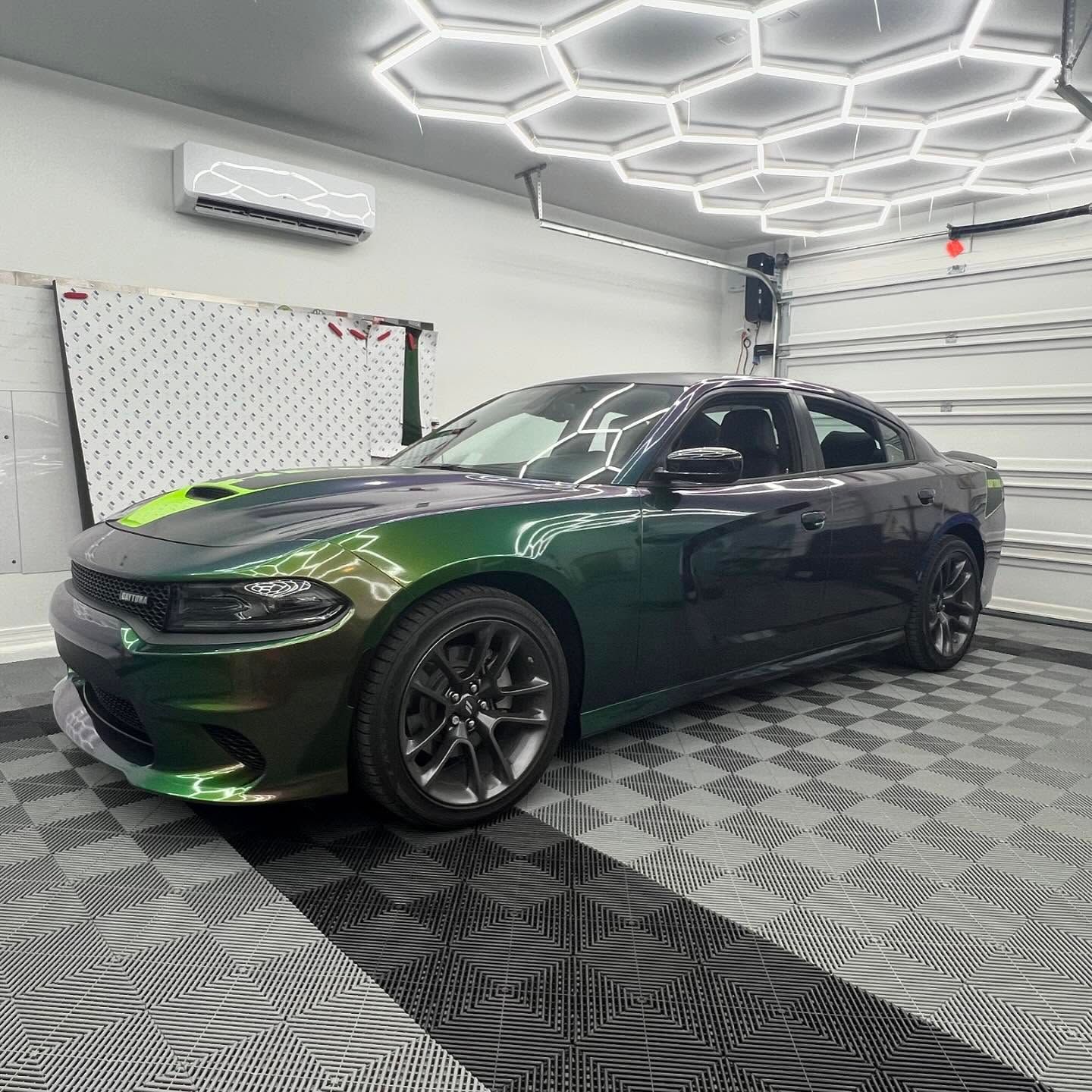 Green and black color-shifting Dodge Charger in a garage with hexagon lights and checkered flooring.