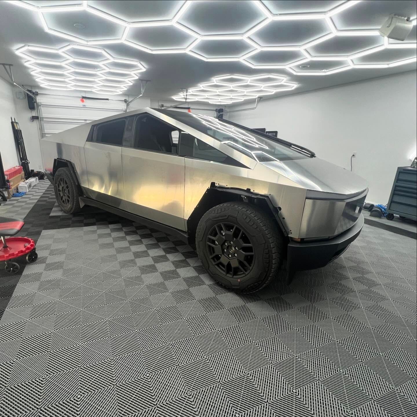 Tesla Cybertruck in a garage with hexagon-shaped lights, gray and black tiled floor, and tools.