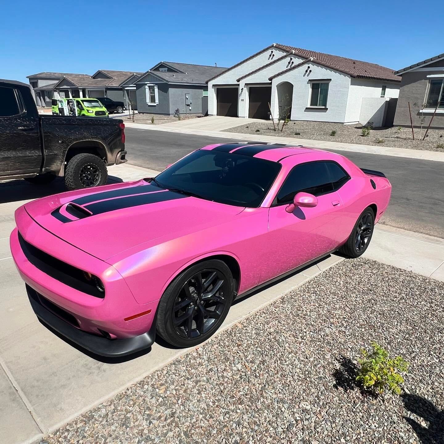 Pink Dodge Challenger with black stripes parked in front of houses.