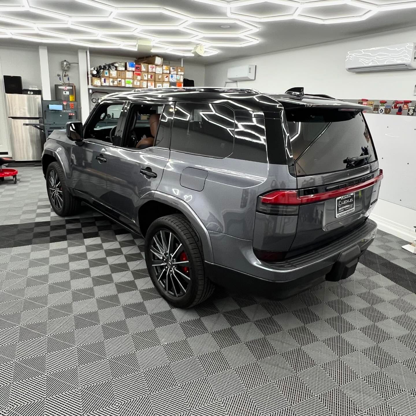 Gray SUV parked in a well-lit shop with black and gray checkered flooring, featuring unique honeycomb ceiling lights.