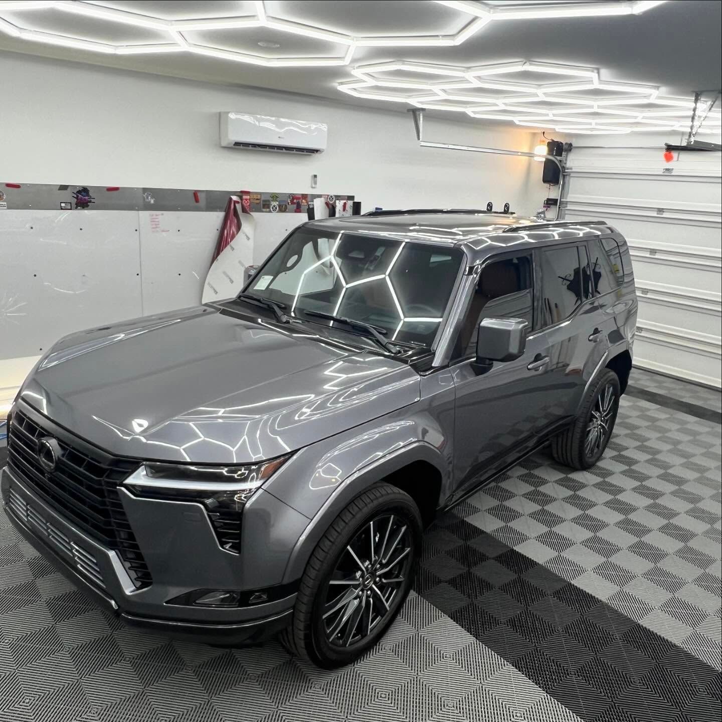 Gray Land Rover Defender in a brightly lit garage with hexagonal lights.