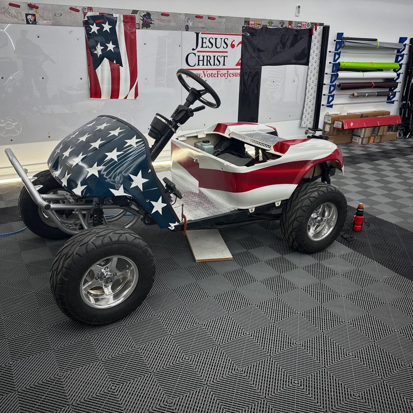 Golf cart customized with an American flag design; red, white, and blue. Garage setting.