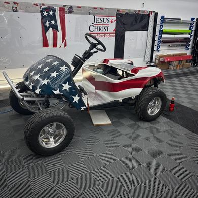Golf cart customized with an American flag design; red, white, and blue. Garage setting.