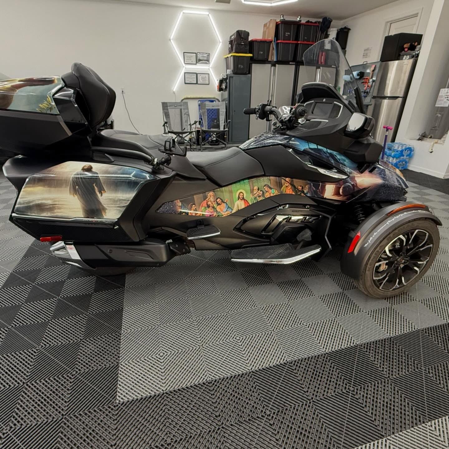 A Can-Am Spyder with a custom wrap featuring a religious scene, parked inside a garage.