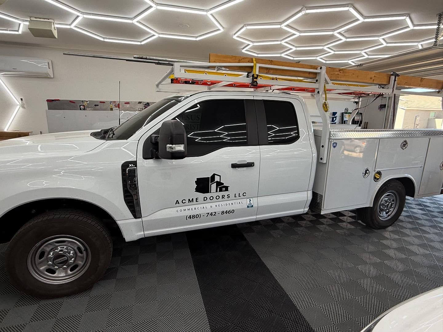 White work truck with company logo parked inside a garage with honeycomb ceiling lights.