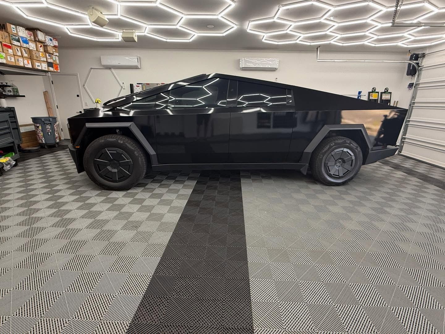 Black Tesla Cybertruck parked in a garage with checkered floor and hexagonal ceiling lights.