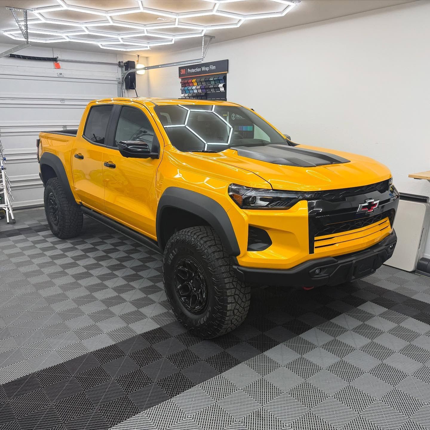 Yellow Chevrolet truck inside a well-lit garage with hexagon ceiling lights and black tire.